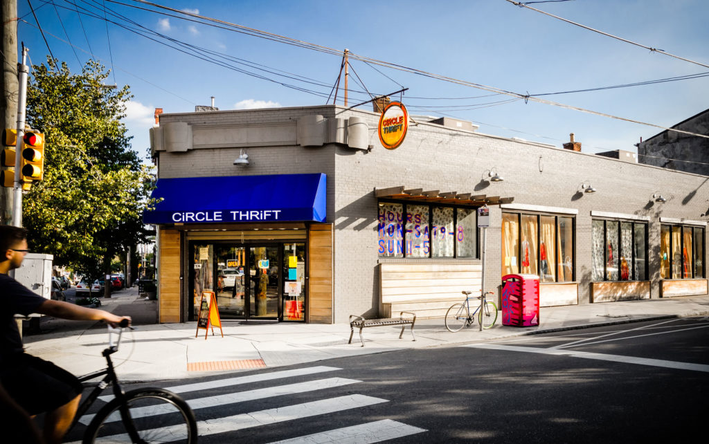 Man riding a bicycle in front of a thrift shop.